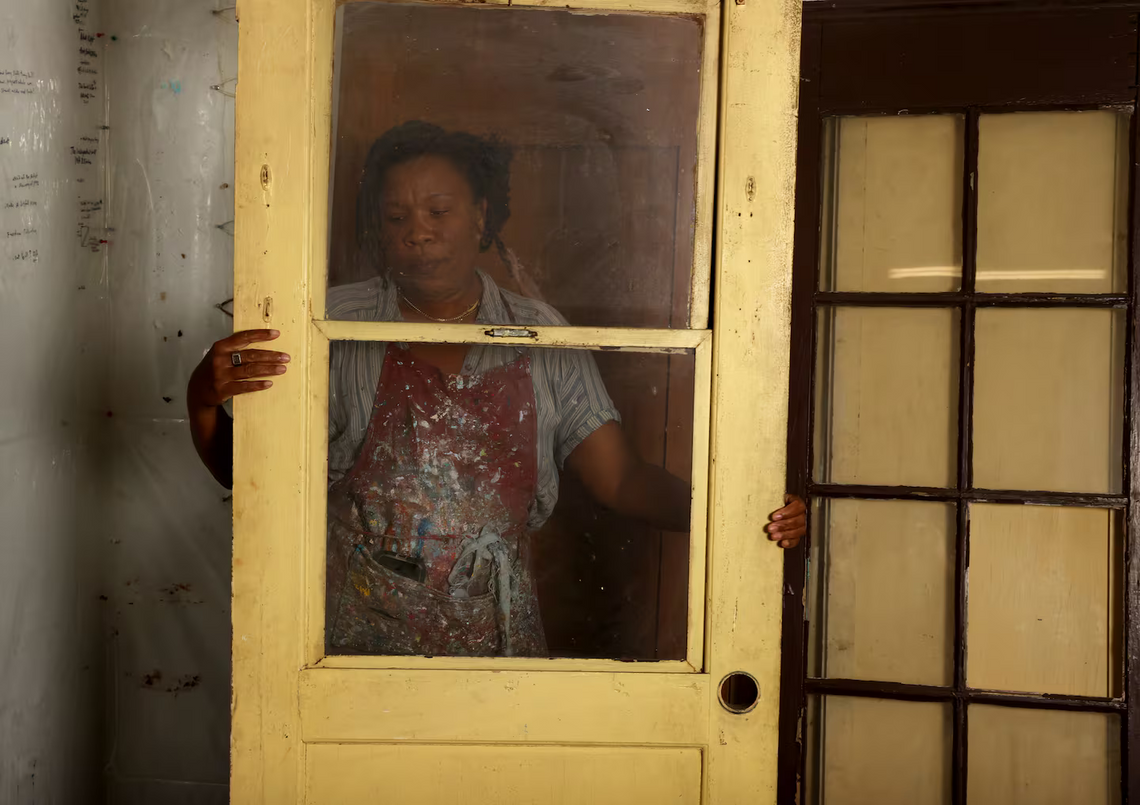 Tomashi Jackson holds a yellow door in her Cambridge, MA studio, she is visible through the two-pane glass.