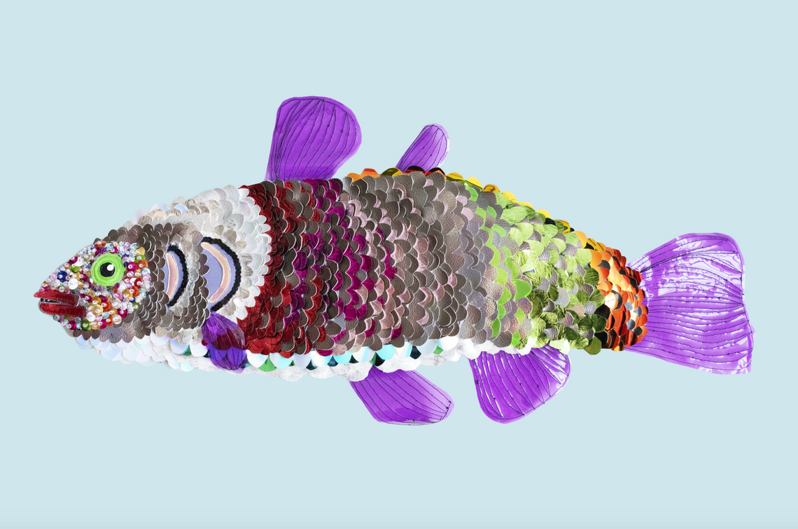 A side view of a sequin-covered fish in colors ranging from magenta, gray, lime green, and orange, with lilac fins and a green eye.