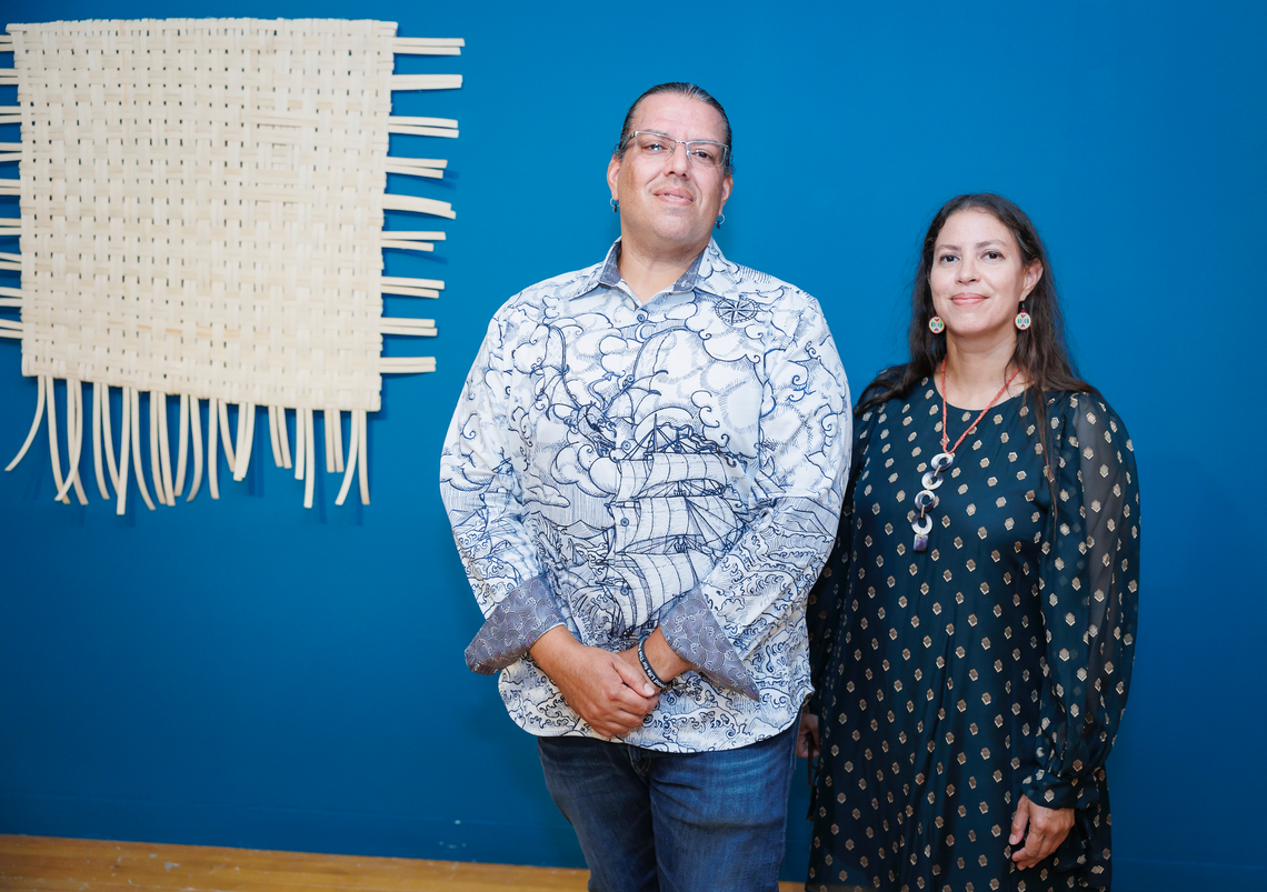 elizabeth and jonathon james-perry standing in front of a blue wall adorned with woven artwork
