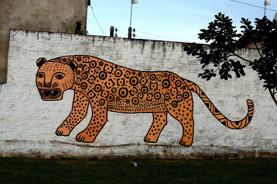 Large orange and black patterned graffiti jaguar painted on a grayish white exterior wall