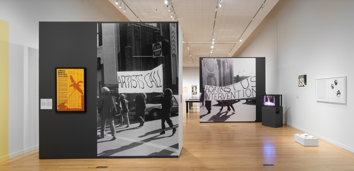 Exhibition entrance with two staggered walls each covered with a large black and white photograph of people marching.