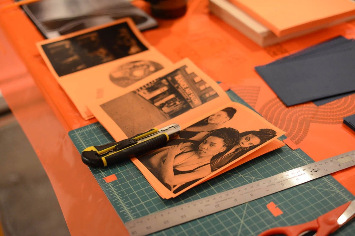 An image of a zine made on orange copy paper with an image of three Black women opposite an image of a storefront on a linoleum cutting pad