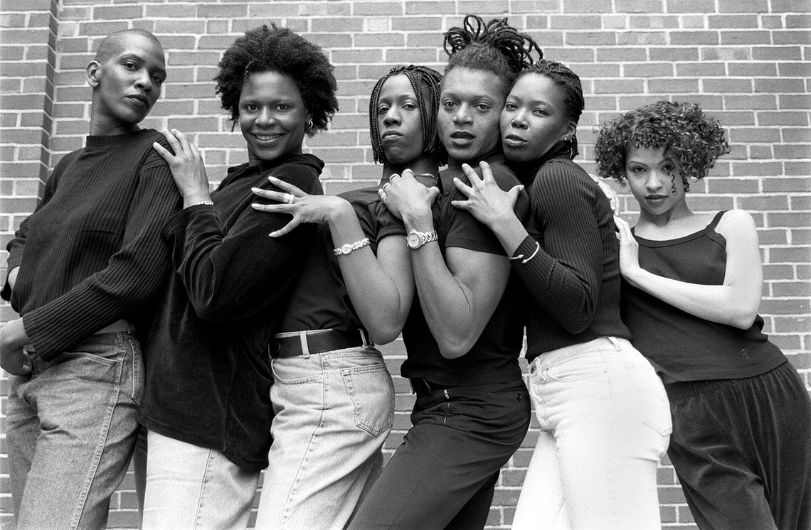 black and white image of 6 people holding eachother's shoulders posing for a camera