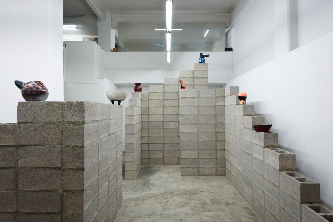 Large gray cinder blocks piled in a white room with delicate pottery pieces on top of the blocks.