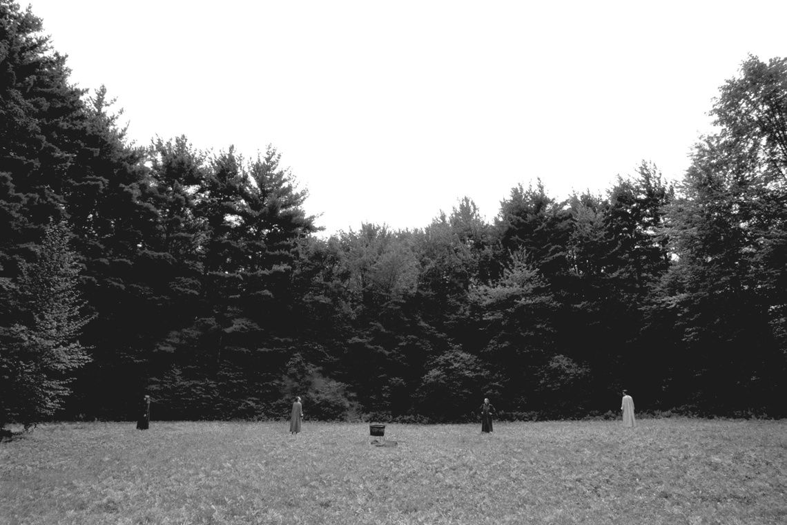 A black and white photograph of Mobius members standing in a open, grassy field surrounded by tall pine trees.