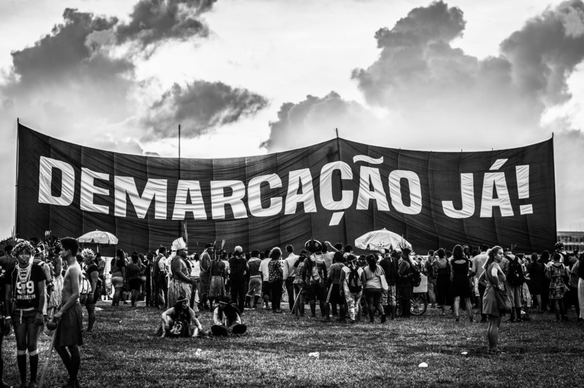 black and white photograph of group of people holding large sign reading demarcacao ja!