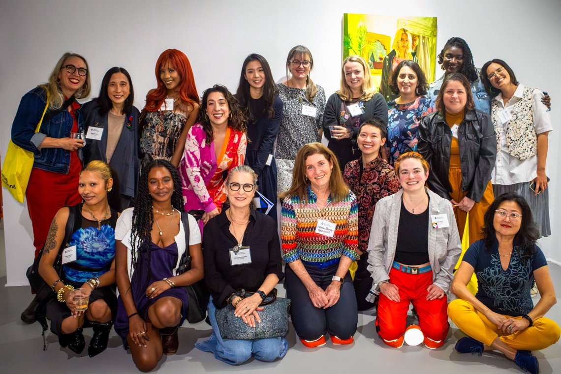 A group of Collective Futures fund grantees pose for a photo in front of a yellow-tinted portrait of a woman in a pink harness.