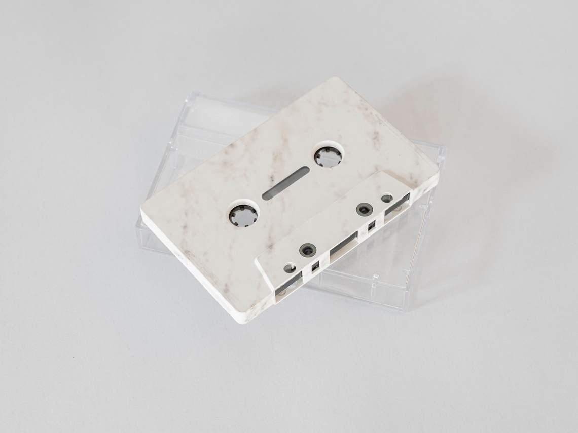 A photograph of a marble cassette tape sitting atop a clear plastic case on a white background.